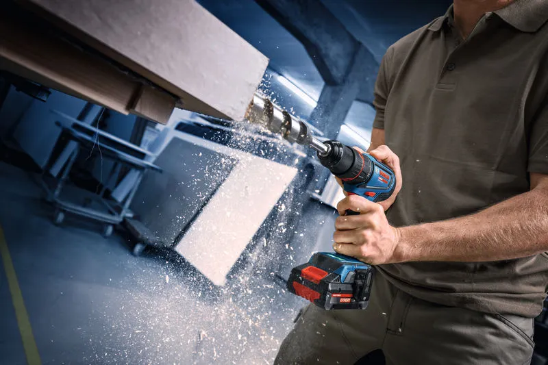 Person borer i træ med en akku-boremaskine, træspåner flyver.